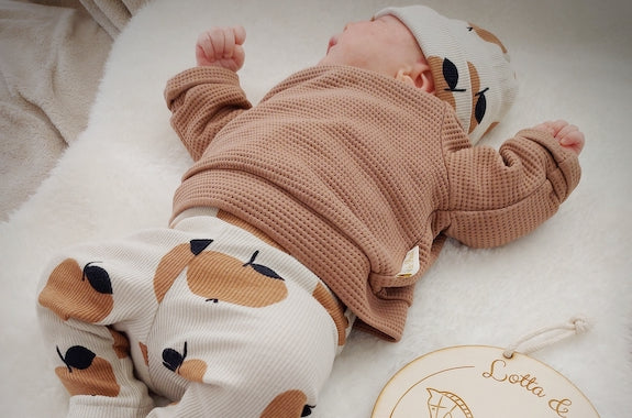 Baby liegt auf dem Rücken. Baby trägt selbstgenähte Kleidung aus Waffelstrick und Ribstrick von Tygdrömmar und Stoffonkel. Stoffe sind von faybee.ch