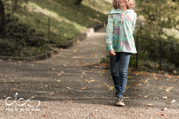 Mädchen läuft auf einer Strasse. Sie trägt einen Sweater aus Biobaumwolle von Faybee.ch